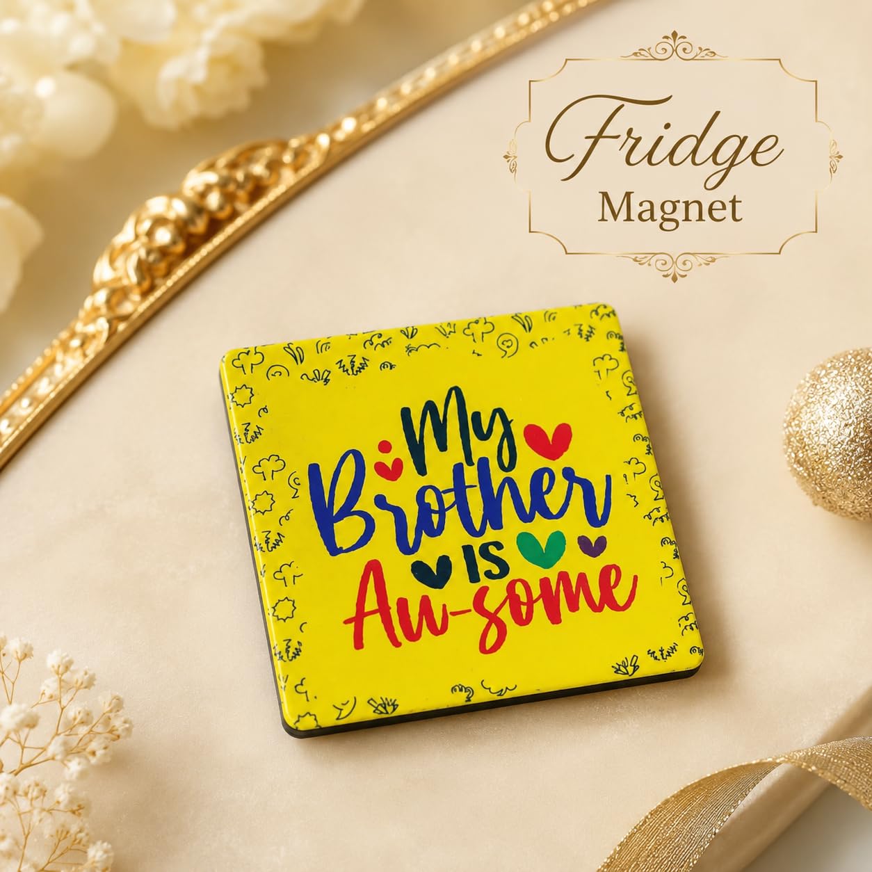 A square yellow fridge magnet with the phrase 'My Brother Is Awesome' in colorful lettering, styled on a beige surface with decorative gold ribbon and holiday ornaments. A label in the top right reads 'Fridge Magnet'.