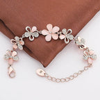 A delicate bracelet with pink flower charms, silver butterfly details, and rhinestone accents, displayed on a brown satin fabric background.