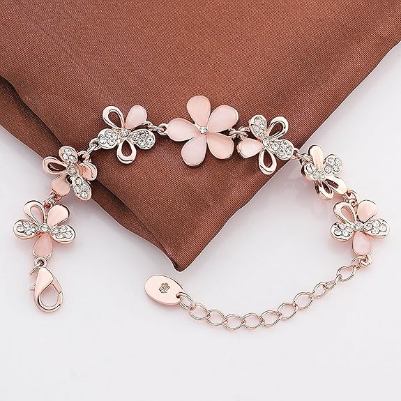 A delicate bracelet with pink flower charms, silver butterfly details, and rhinestone accents, displayed on a brown satin fabric background.
